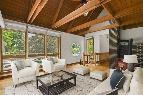 living room with light wood-type flooring, a ceiling fan, vaulted ceiling with beams, and a wood stove