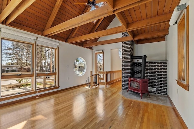 interior space with a wood stove, lofted ceiling with beams, baseboards, light wood-style floors, and a ceiling fan