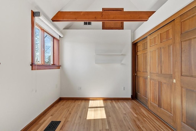 unfurnished bedroom featuring lofted ceiling with beams, baseboards, and light wood-style floors