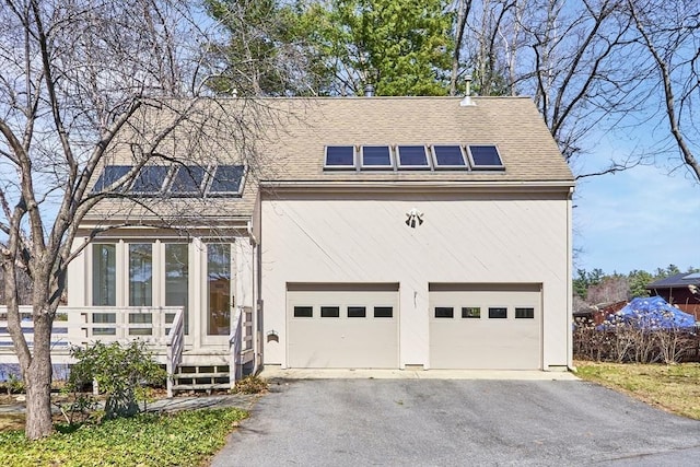 view of front of house with solar panels, roof with shingles, and driveway