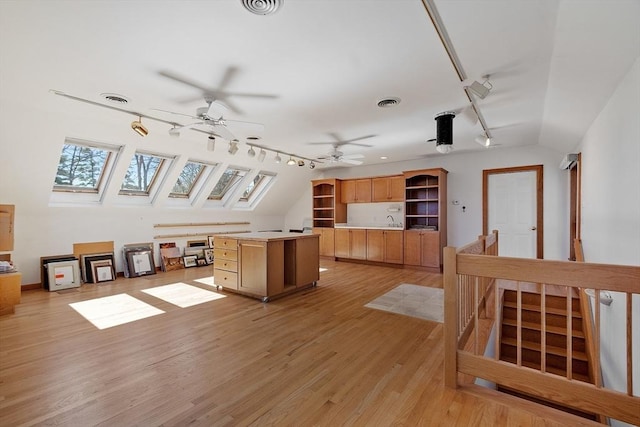 interior space featuring a kitchen island, open shelves, light wood-style flooring, visible vents, and lofted ceiling with skylight