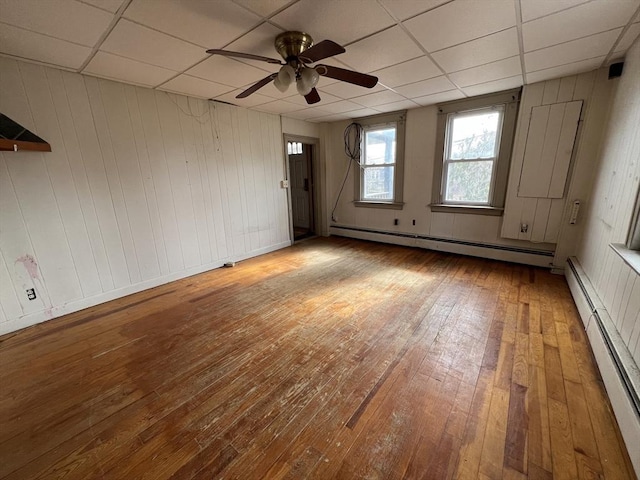 empty room featuring wood-type flooring, a drop ceiling, and baseboard heating