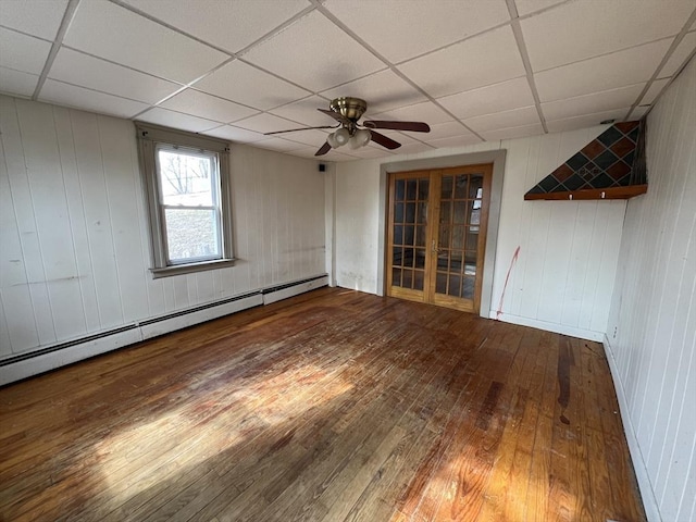 empty room featuring ceiling fan, hardwood / wood-style floors, french doors, a paneled ceiling, and a baseboard heating unit