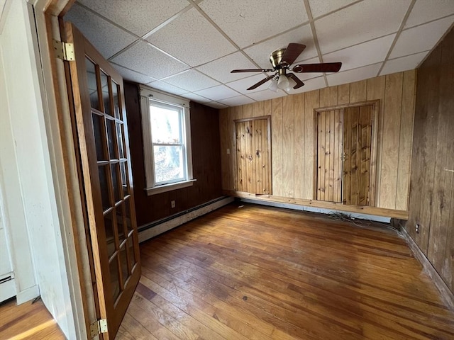 spare room featuring a baseboard radiator, a drop ceiling, wood walls, and hardwood / wood-style flooring