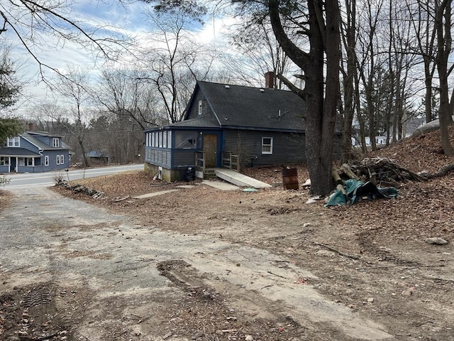 exterior space with driveway, a shingled roof, and a chimney