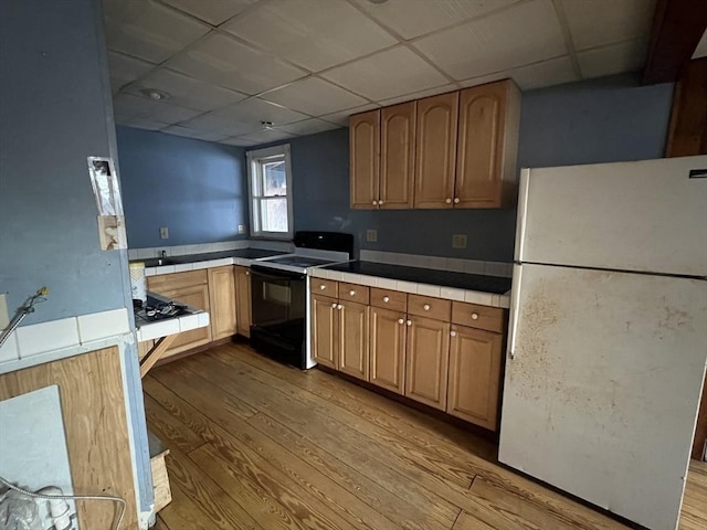 kitchen featuring tile counters, electric range, light wood-type flooring, and freestanding refrigerator