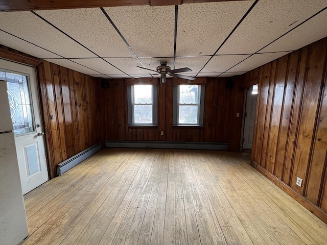 spare room with a baseboard heating unit, a ceiling fan, light wood-style flooring, and wooden walls