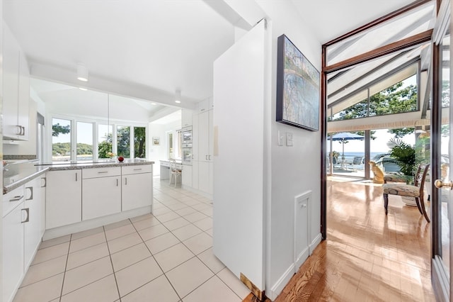 kitchen with white cabinets, vaulted ceiling, oven, and light tile patterned floors