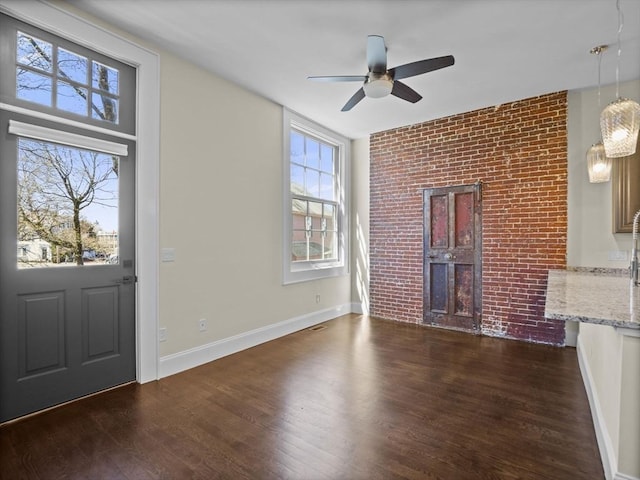 unfurnished living room featuring baseboards, a ceiling fan, dark wood-style floors, and brick wall