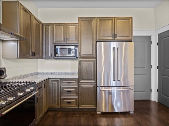 kitchen featuring light stone counters, dark wood-style flooring, wall chimney range hood, and stainless steel appliances