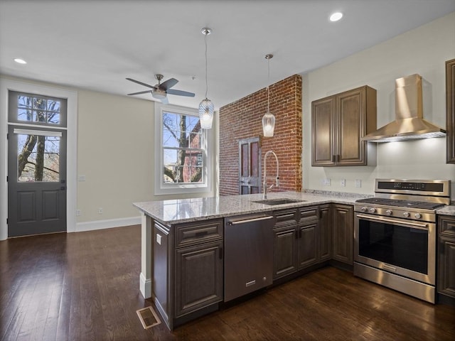 kitchen with a sink, stainless steel appliances, wall chimney exhaust hood, a peninsula, and visible vents