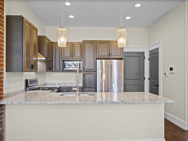 kitchen featuring a peninsula, light stone counters, appliances with stainless steel finishes, and dark wood-style flooring