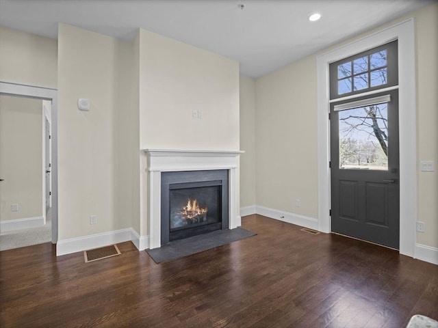 interior space with a fireplace with flush hearth, wood finished floors, visible vents, and baseboards