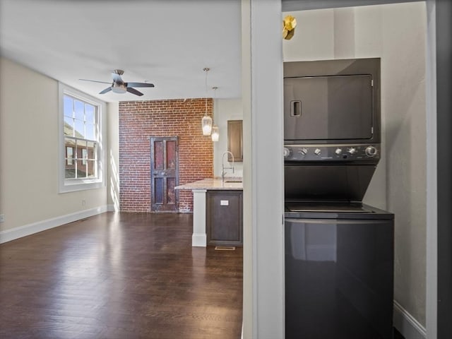 laundry area with dark wood finished floors, stacked washer / dryer, laundry area, a sink, and ceiling fan