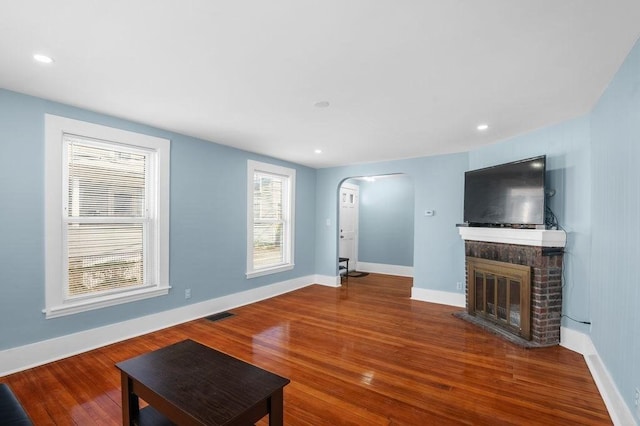 unfurnished living room featuring arched walkways, baseboards, a fireplace, and wood finished floors