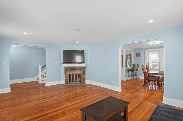 living area featuring stairway, arched walkways, a fireplace, and wood finished floors