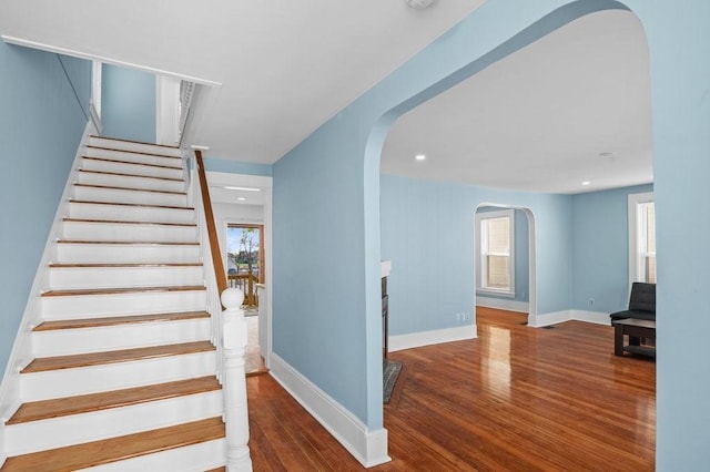 stairway featuring arched walkways, baseboards, recessed lighting, and wood finished floors