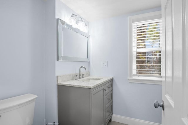 half bath with baseboards, vanity, and toilet