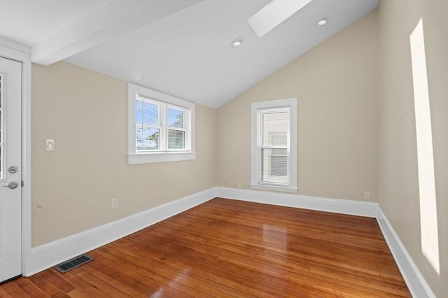spare room featuring vaulted ceiling with skylight, visible vents, baseboards, recessed lighting, and hardwood / wood-style floors