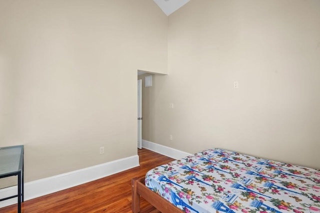bedroom featuring baseboards, wood finished floors, and lofted ceiling
