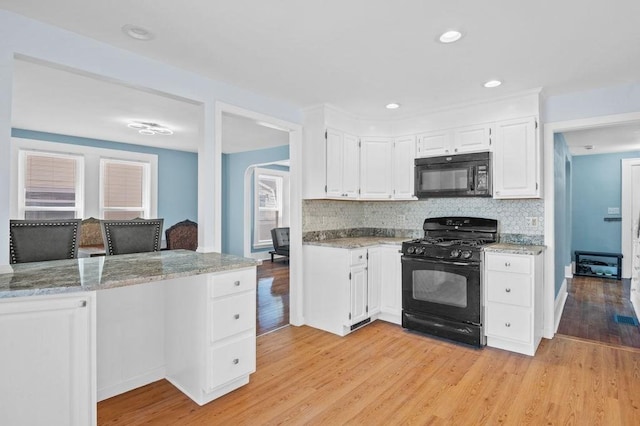 kitchen with decorative backsplash, light wood-type flooring, white cabinetry, light stone counters, and black appliances