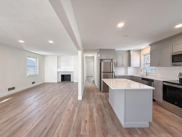 kitchen with a large fireplace, stainless steel appliances, gray cabinetry, and a center island