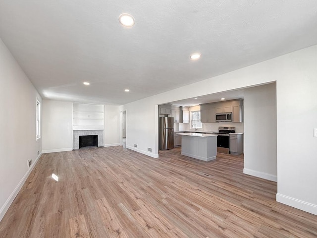 unfurnished living room featuring sink, a fireplace, light wood-type flooring, and built in shelves