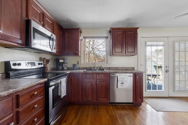 kitchen featuring dark wood finished floors, reddish brown cabinets, stainless steel appliances, and a sink