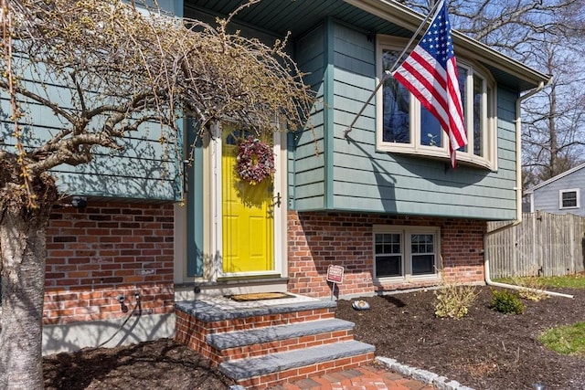 view of exterior entry with fence and brick siding