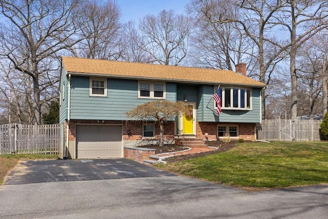 bi-level home featuring a front lawn, a chimney, fence, and aphalt driveway