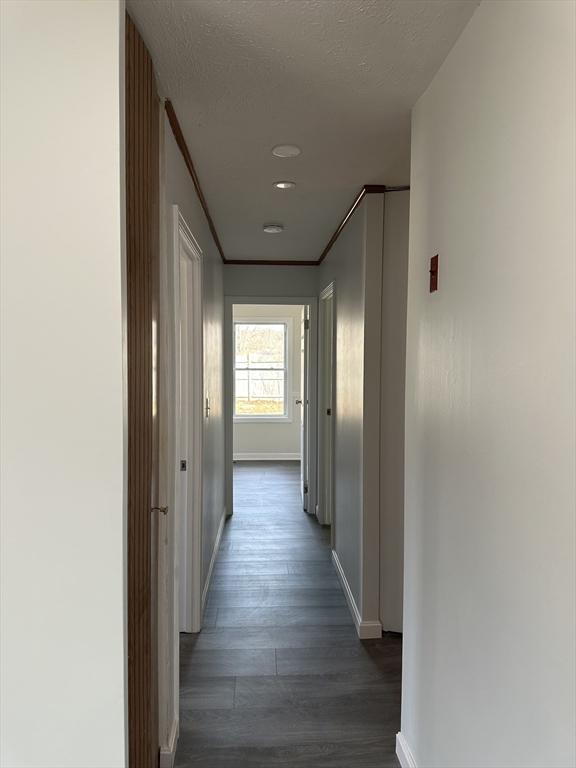 corridor featuring dark wood-style floors, crown molding, baseboards, and a textured ceiling