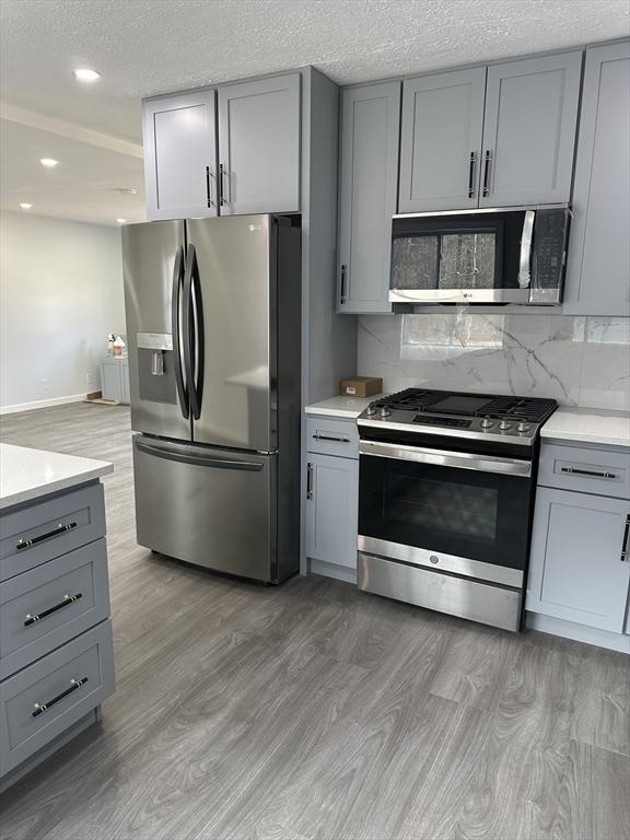 kitchen featuring gray cabinets, light countertops, light wood finished floors, stainless steel appliances, and decorative backsplash