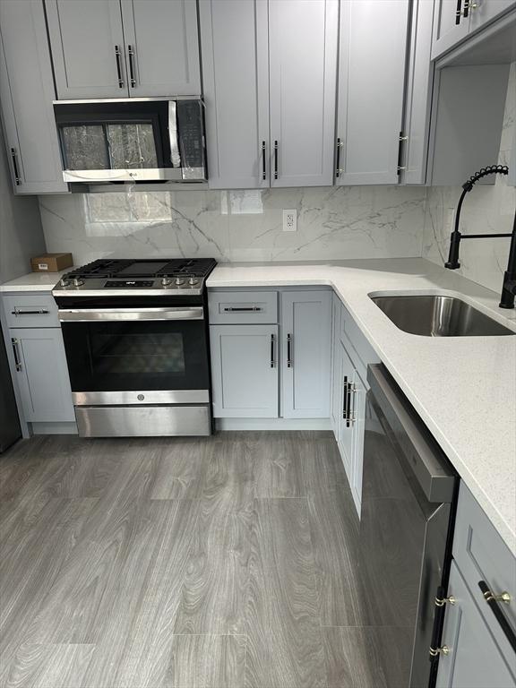 kitchen featuring light countertops, tasteful backsplash, appliances with stainless steel finishes, a sink, and gray cabinets
