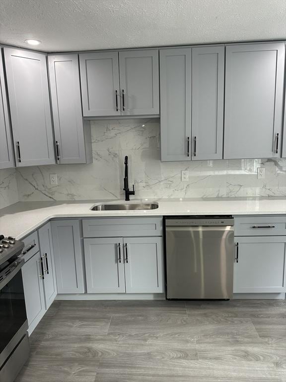 kitchen with gray cabinets, a sink, light wood finished floors, stainless steel appliances, and decorative backsplash