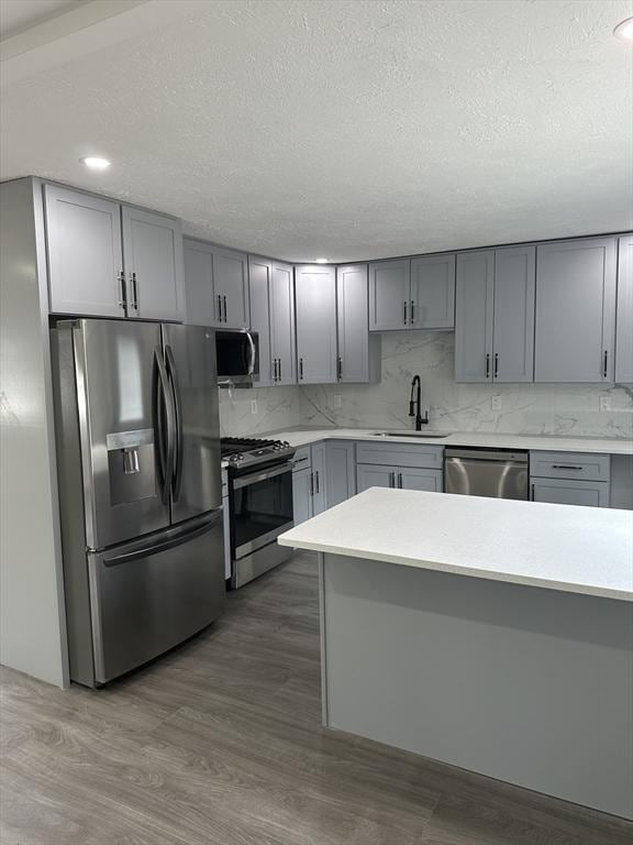 kitchen featuring decorative backsplash, light countertops, stainless steel appliances, a sink, and gray cabinetry
