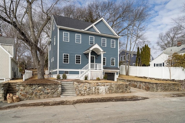 colonial-style house featuring a garage, roof with shingles, and fence