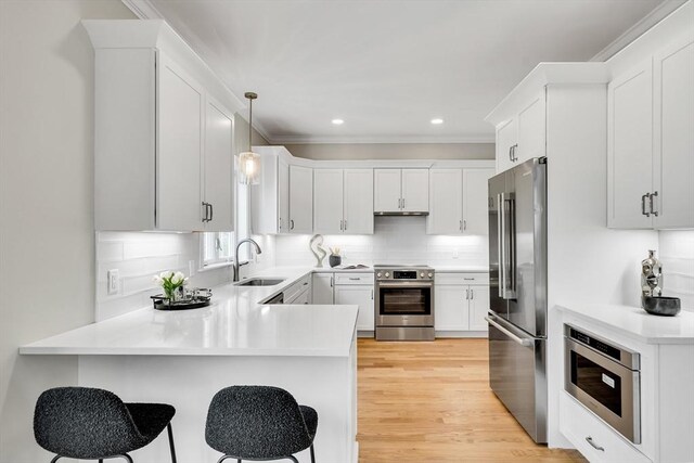 kitchen featuring tasteful backsplash, light countertops, appliances with stainless steel finishes, a sink, and a peninsula