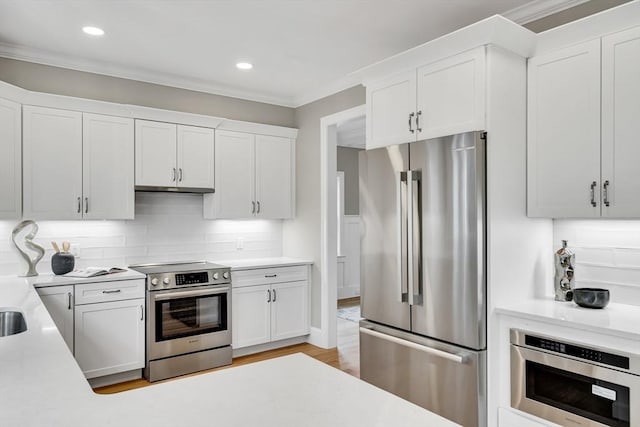 kitchen featuring tasteful backsplash, white cabinets, ornamental molding, stainless steel appliances, and light countertops