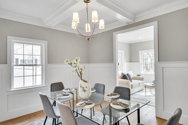 dining area with beam ceiling, a wainscoted wall, light wood-style flooring, and an inviting chandelier