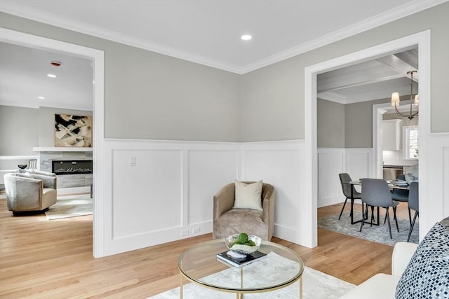 sitting room with recessed lighting, a notable chandelier, light wood-type flooring, a glass covered fireplace, and crown molding