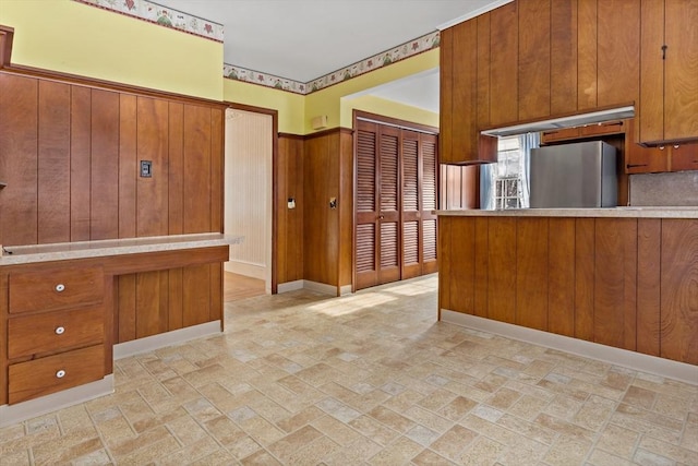 kitchen featuring kitchen peninsula, wood walls, and stainless steel refrigerator