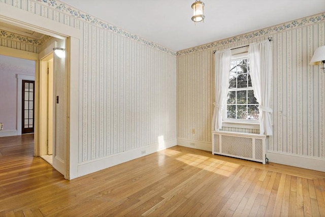 unfurnished room featuring radiator heating unit and hardwood / wood-style floors