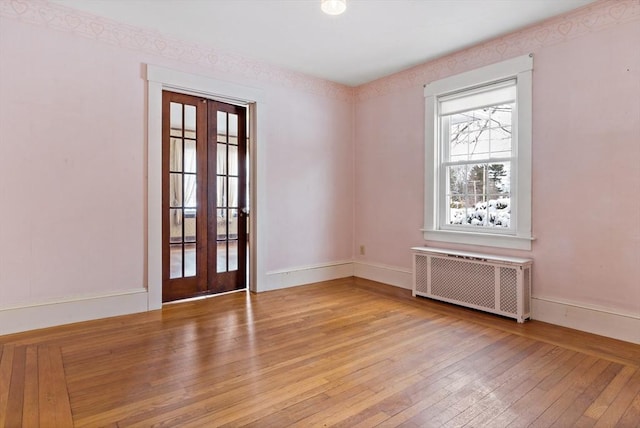 empty room with radiator heating unit, light hardwood / wood-style flooring, and french doors