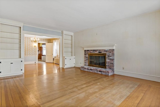 unfurnished living room featuring crown molding, light hardwood / wood-style floors, a chandelier, a brick fireplace, and built in shelves