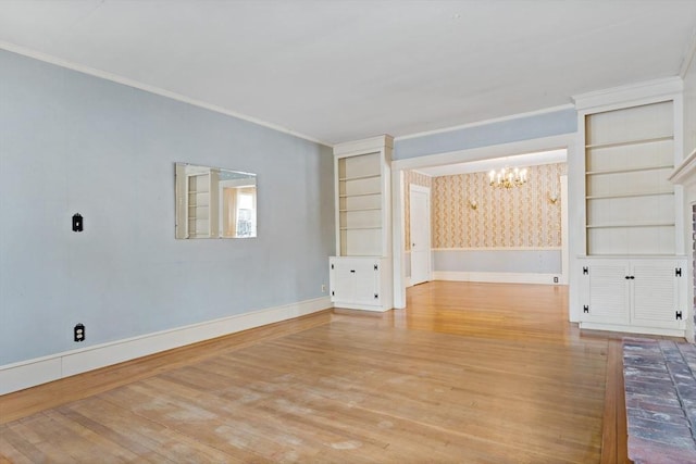 spare room with built in shelves, light hardwood / wood-style flooring, crown molding, and an inviting chandelier