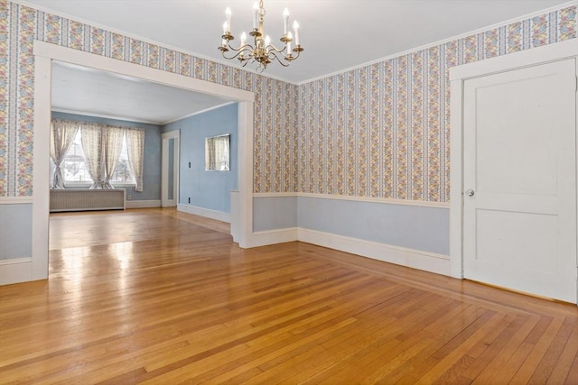 spare room with a notable chandelier, radiator heating unit, ornamental molding, and wood-type flooring