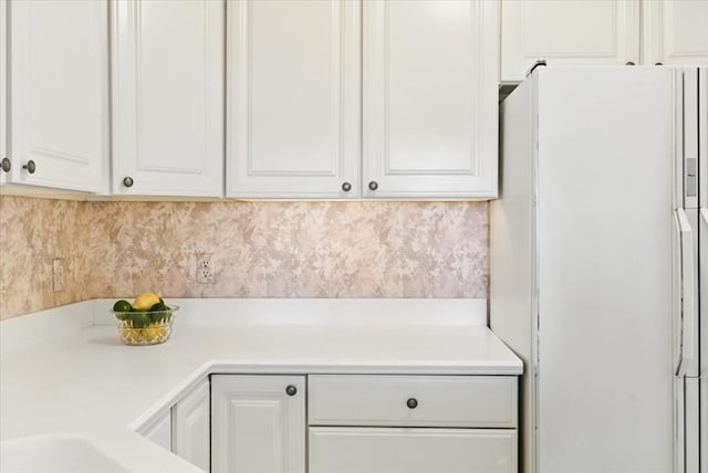 kitchen with light countertops, freestanding refrigerator, backsplash, and white cabinetry