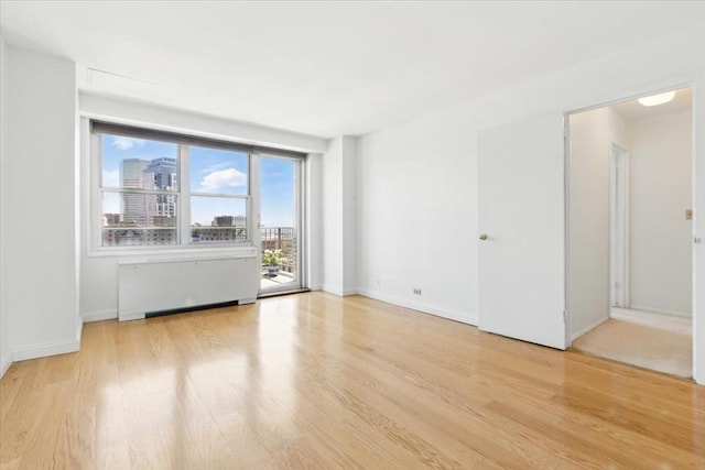 spare room with radiator heating unit, baseboards, and wood finished floors