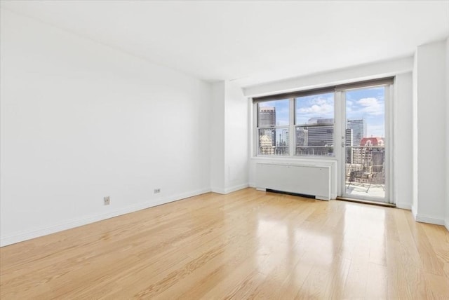 spare room with light wood-type flooring, radiator, and baseboards