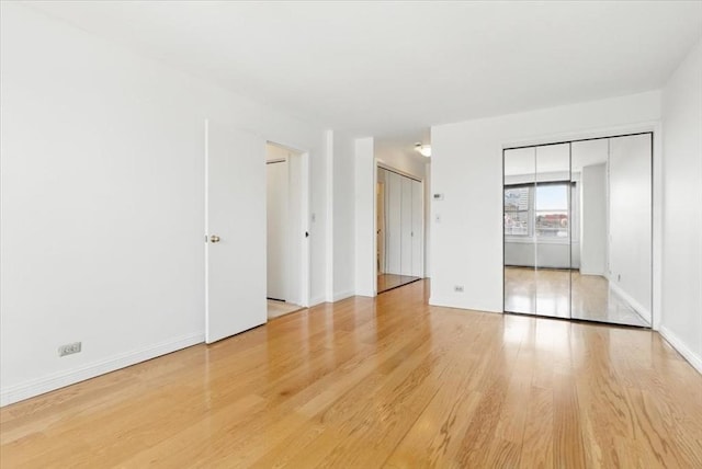 unfurnished bedroom featuring baseboards, multiple closets, and wood finished floors